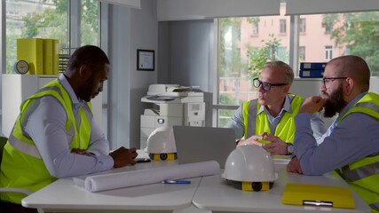 Multiethnic team of construction workers sitting in office and collaborating