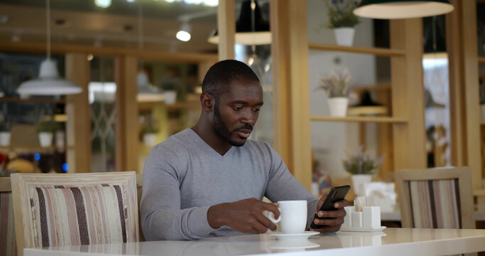 Portrait of mixed-race man sitting at table with cup of coffee and using smartphone in cafe - Powered by Adobe