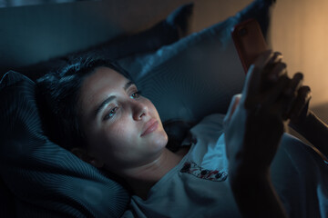 Fototapeta na wymiar Young woman lying in bed and using her smartphone