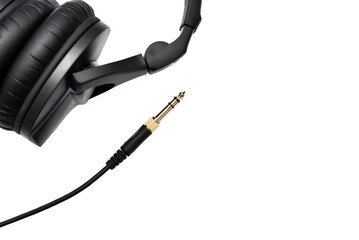 Stereo audio jack with cable with blurred headphones on white background with copy space for text. Gold jack plug for connecting headphone.