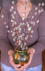 Mom grandma holds willow trees in a green vase standing indoors, holding with two hands, Christianity holiday, mom's hands, grandmother's hands, adult woman's hands