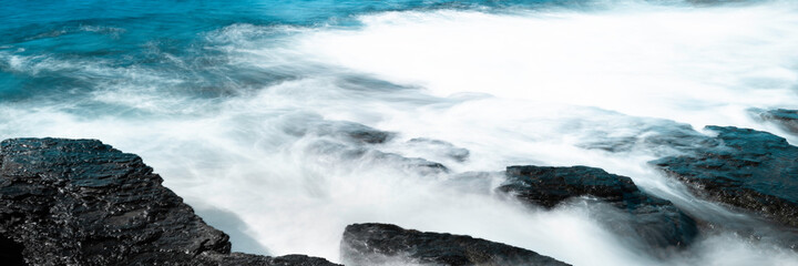 Fototapeta na wymiar Misty Ocean Waves Seascape. Speed Motion Water over Rocks Background. Curving Wave Lines Swirling into White Lights. Panoramic Horizontal close-up with Space for Text or Design.