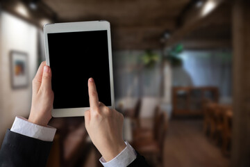 Hand holding tablet with blank white screen in cafe.