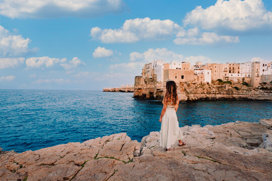 Young girl in front of the village of Polignano a Mare, sky with white clouds