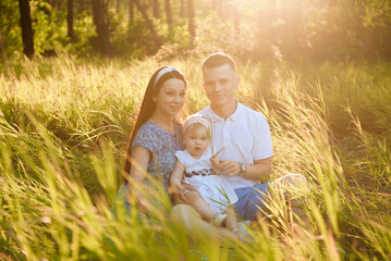 Fototapeta premium Happy family dad, mom playing in the fresh air on the field watching the beautiful emotional sunset in the backlight