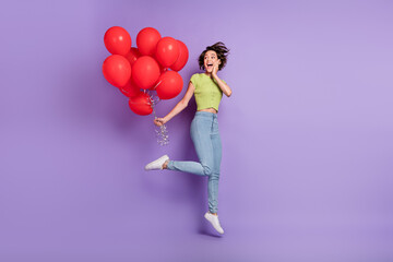 Fototapeta na wymiar Photo of beautiful attractive excited emotion young woman dressed green t-shirt holding red air balls jumping high isolated purple color background