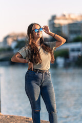 Young caucasian woman with sunglasses standing next to a river during sunset