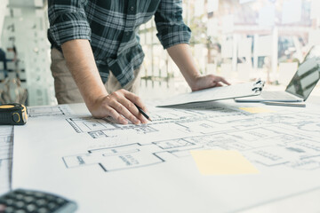 Interior designer or architect reviewing blueprints and holding pencil drawing on desk at home...