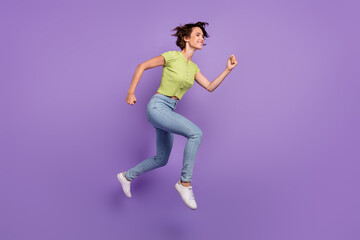 Fototapeta na wymiar Photo of positive funky young woman dressed green t-shirt jumping high running fast looking empty space isolated purple color background