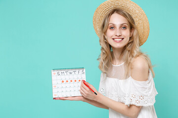 Smiling young woman girl in white dress hat hold periods calendar for checking menstruation days red pencil isolated on blue turquoise wall background studio. Medical healthcare gynecological concept.