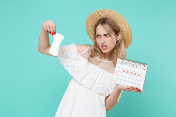 Disgusted young woman girl in white dress hat hold periods calendar for checking menstruation days...