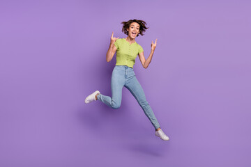 Fototapeta na wymiar Photo of sweet rude young woman dressed green t-shirt jumping showing hard rock signs isolated purple color background