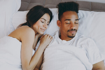 Top view beautiful young couple two family in casual white clothes lying in bed sleep woman hands folded under head on man shoulder relax spend time together in bedroom lounge home in own room house.