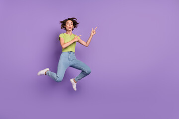 Fototapeta na wymiar Photo of pretty impressed young lady wear green t-shirt pointing fingers empty space jumping isolated violet color background