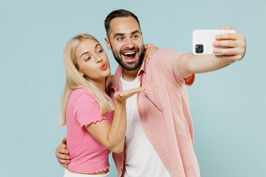 Young fun couple two friends family man woman in casual clothes doing selfie shot on mobile cell phone post photo blow air kiss together isolated on pastel plain light blue background studio portrait.