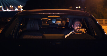 Man using mobile phone sitting in car outdoors at night