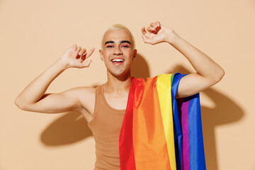 Young smiling happy blond latin gay man with make up in beige tank shirt with rainbow flag on...