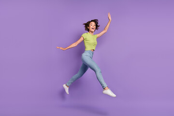 Fototapeta na wymiar Photo of charming excited young woman dressed green t-shirt jumping walking waving arm empty space isolated purple color background