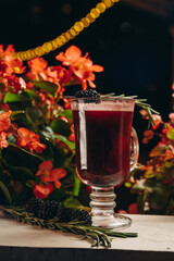 Blackberry mulled wine with rosemary in a glass cup on flowers background