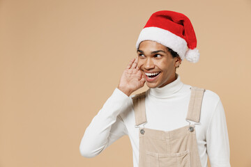Young curious african man 20s wear Santa Claus red Christmas hat try to hear you overhear listening...
