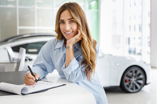 Happy woman customer female buyer client in blue shirt sign agreement document choose auto want to buy new automobile in car showroom vehicle salon dealership store motor show indoor. Sales concept.
