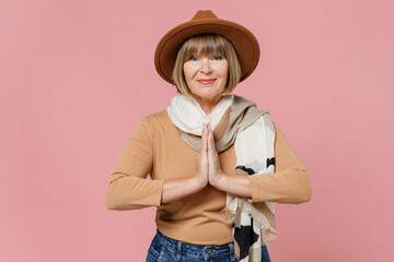 Traveler tourist fascinating mature elderly senior lady woman 55 years old wears brown shirt hat scarf hands folded in prayer gesture isolated on plain pastel light pink background studio portrait