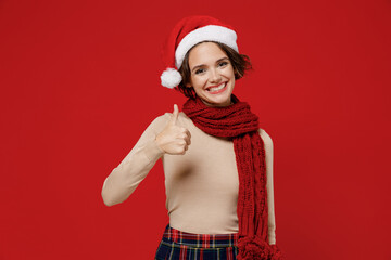 Young smiling happy satisfied caucasian woman wear Santa Claus Christmas red hat showing thumb up like gesture isolated on plain red background studio portrait Happy New Year 2022 celebration concept