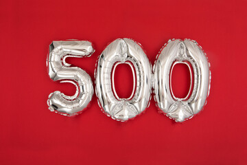 Silver balloon showing number 500 on red background. From above of silver shiny balloons...