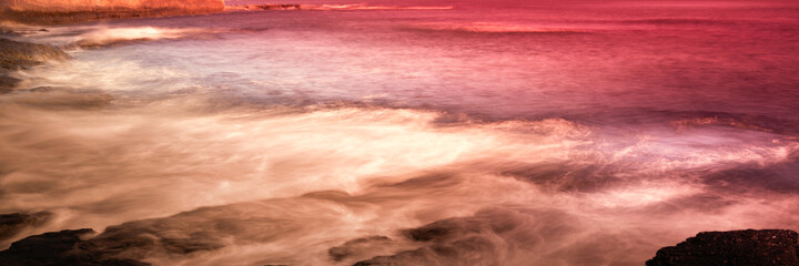 Stormy seascape with ocean waves flowing over the rocks. Panoramic close-up rocky beach landscape with space for text or design.