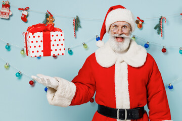 Old fun Santa Claus man in Christmas hat red suit throws up present box with gift ribbon bow isolated on plain blue background studio Happy New Year 2022 celebration merry ho x-mas holiday concept.