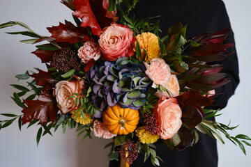 Rich bouquet with autumn flowers and a pumpkin in the hands of a girl on a light background. Bright...