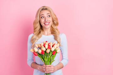 Photo of charming happy dreamy young woman look empty space hold flowers isolated on pink color background