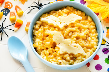 Fun Food for kids - Halloween pumpkin risotto with cinnamon decorated with bat shaped pieces of cheese and festive decorations like spiders, corn candies and pumpkins