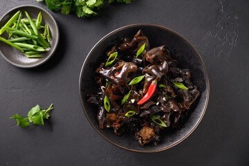 Chinese tree ear black muer mushrooms with chilli pepper and coriander on dark black background. View from above.