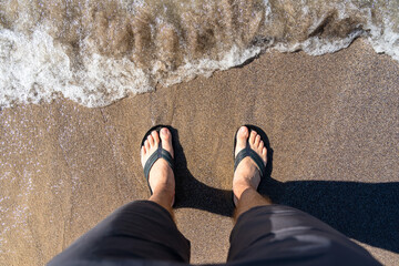 Male's feet on slippers on the beach. Relax on the sand