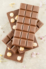 Milk chocolate bar with whole hazelnut kernels, flowers on white background. Healthy food concept, delicious chocolate sweets for kids, diet, sugar