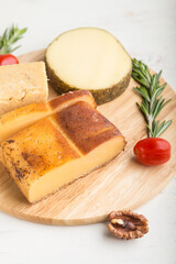 Smoked cheese and various types of cheese with rosemary and tomatoes on wooden board on a white background . Side view, selective focus.