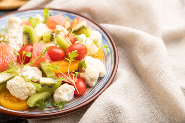 Vegetarian salad of cauliflower cabbage, kiwi, tomatoes, microgreen sprouts on black concrete background. Side view, selective focus.