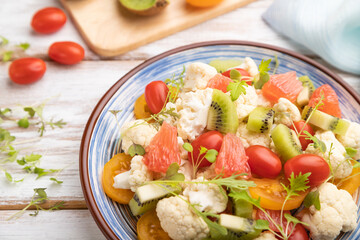 Vegetarian salad of cauliflower cabbage, kiwi, tomatoes, microgreen sprouts on gray wooden background. Side view, selective focus.