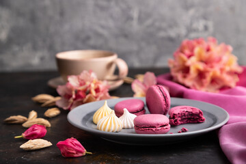 Fototapeta na wymiar Purple macarons or macaroons cakes with cup of coffee on a black concrete background. Side view, selective focus.