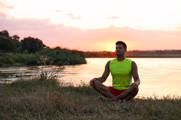 Fototapeta premium Man meditating near river in twilight. Space for text