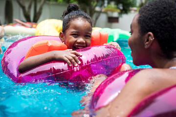 Closeup of black mother and daughter enjoying the pool with inflatable tubes - obrazy, fototapety, plakaty