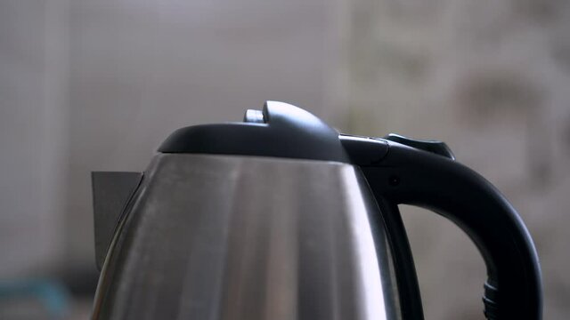 electric kettle. Boiling water and steam comes out of silver modern kettle. An electric kettle boils water. Person turns on the electric kettle