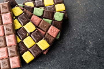 Multicolored fruit chocolate bars on black background. Handmade chocolate with mint, mango, orange, strawberry flavor. Healthy food concept, delicious chocolate sweets for kids, diet, sugar