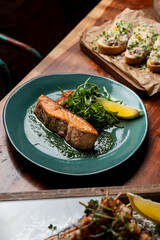 Healthy salmon steak with vegetables on wooden table in a restaurant, soft shadows, dark place