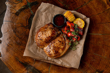 Top view of golden t-bone steak with vegetables and bbq sauce on wooden table