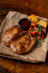 Top view of golden t-bone steak with vegetables and bbq sauce on wooden table
