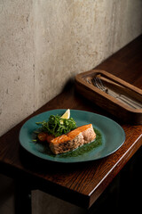 Healthy salmon steak with vegetables on wooden table in a restaurant, soft shadows, dark place