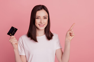Photo of young pretty girl hold bank card point finger empty space ad promo select sale isolated over pink color background
