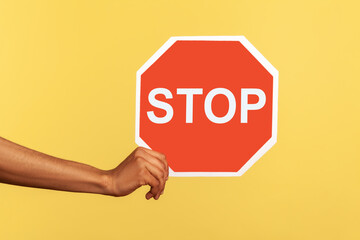 Closeup of male hand holding octagonal red Stop symbol, ban concept, arm showing traffic sign,...